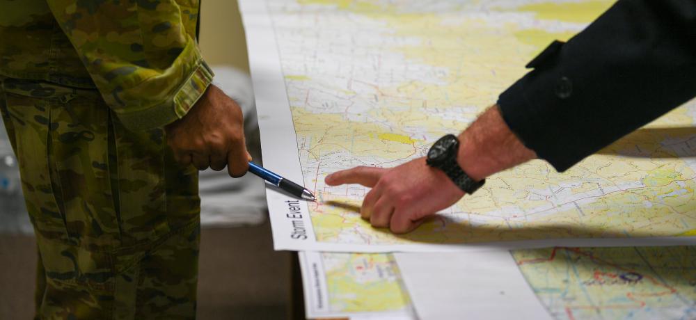 Victoria’s Joint Task Group Task Unit Commanding Officer Lieutenant Colonel Scott D’Rozario points at a map as Shire Municipal Emergency Management Officer Travis Dixon, briefs him about the situation and possible needs of the communities around Trentham and other storm affected areas in Central Victoria.