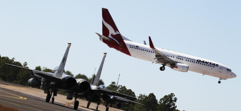 Two Republic of Singapore Air Force F-15 aircraft wait on the taxiway as a passenger plane lands at Darwin airport.