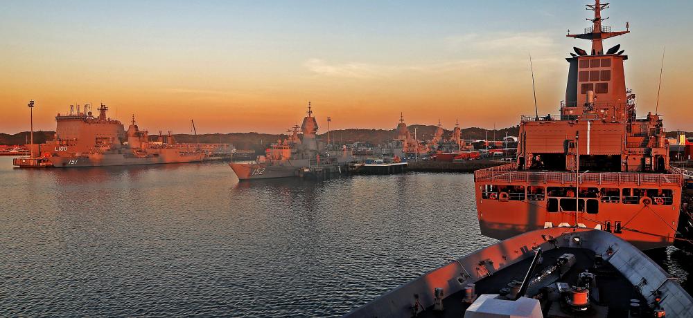HMAS Choules, HMAS Stuart, HMAS Arunta, HMAS Warramunga, HMAS Toowoomba, HMAS Stalwart and the forecastle of HMAS Hobart in the foreground alongside Fleet Base West as the sun rises
