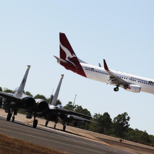 Two Republic of Singapore Air Force F-15 aircraft wait on the taxiway as a passenger plane lands at Darwin airport.