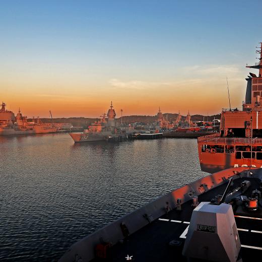HMAS Choules, HMAS Stuart, HMAS Arunta, HMAS Warramunga, HMAS Toowoomba, HMAS Stalwart and the forecastle of HMAS Hobart in the foreground alongside Fleet Base West as the sun rises